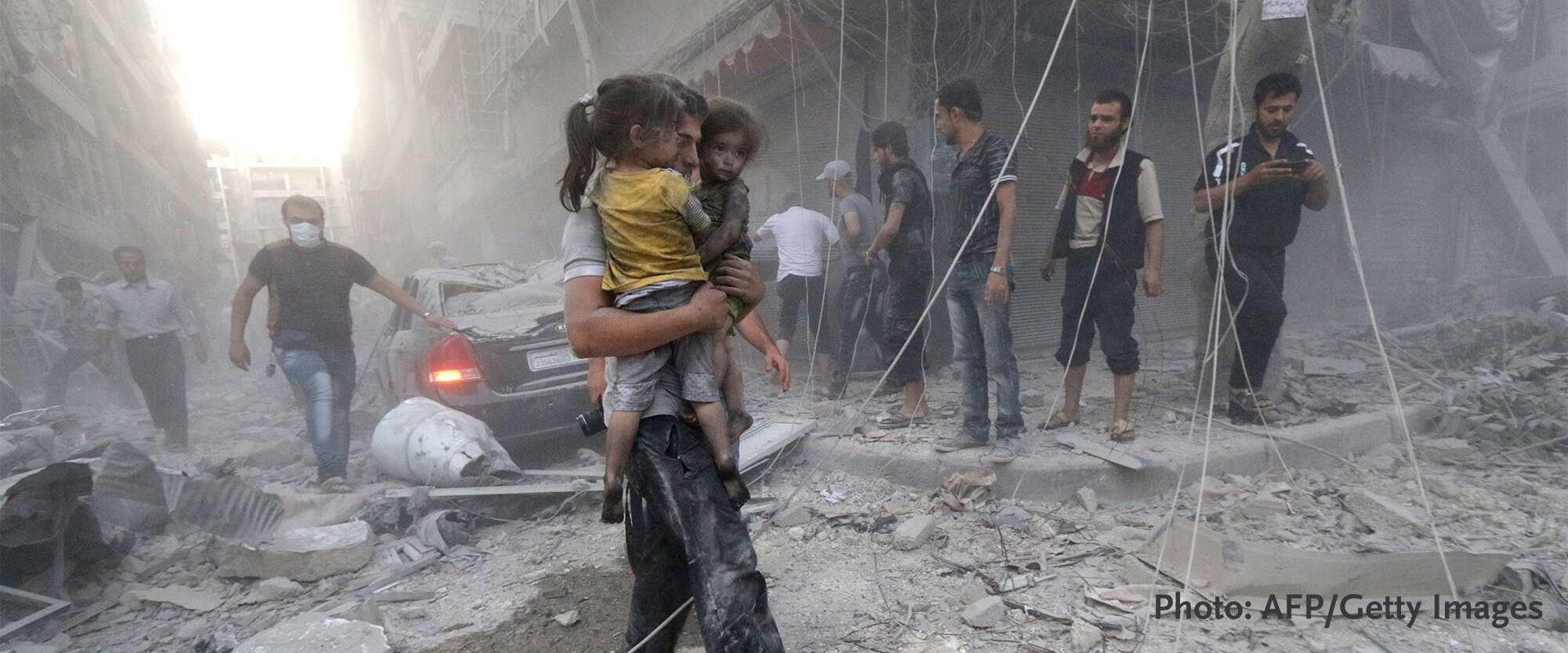 Syrian man carrying child through building rubble in Syria